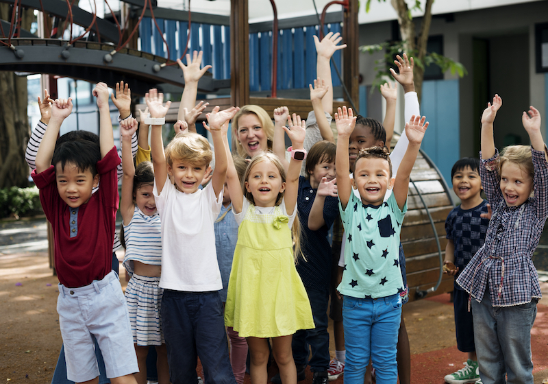 alternative teacher certification program graduate without a teaching degree standing with happy students in a playground